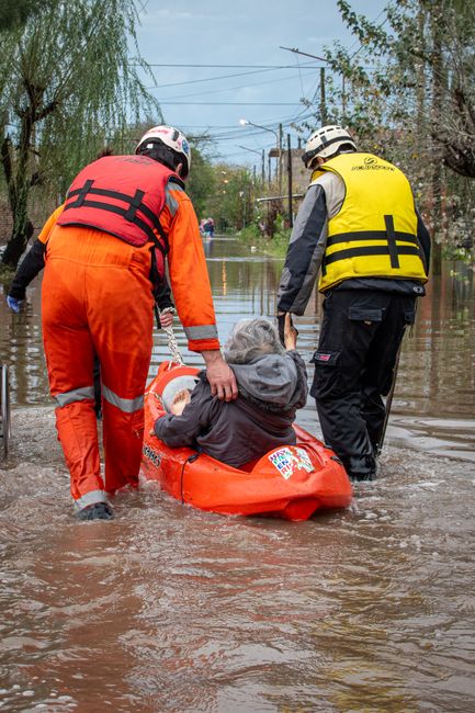 A flooded city street in Croydon Waddon during daytime, with water covering the entire road and partially submerging vehicles and pedestrians. Multi-storey buildings with colorful facades, including p